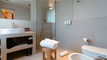 A modern bathroom with a glass shower enclosure, a white sink, and a wooden stool with towels.