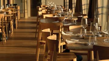 A restaurant with wooden tables and chairs, arranged in rows, with empty wine glasses and plates on the tables.