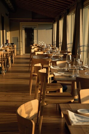 A restaurant with wooden tables and chairs, arranged in rows, with empty wine glasses and plates on the tables. - HEMANAIRE (Cremolino)