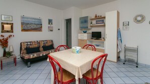 A room with a dining table, red chairs, a sofa, a television, and shelves with decorative items. - N043 - Numana, two-room apartment with garden (Sirolo)