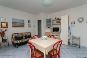 A room with a dining table, red chairs, a sofa, a television, and shelves with decorative items.
