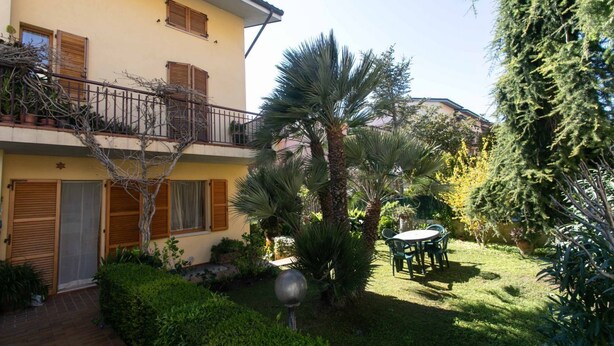 A two-story building with a balcony, a patio with a table and chairs, and various plants. - N043 - Numana, two-room apartment with garden (Sirolo)