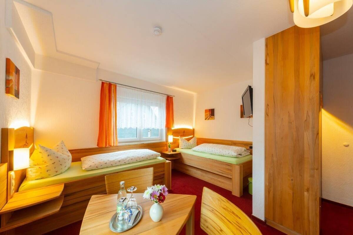 A compact hotel room with two single beds, a small table with a tray, and a window with curtains.