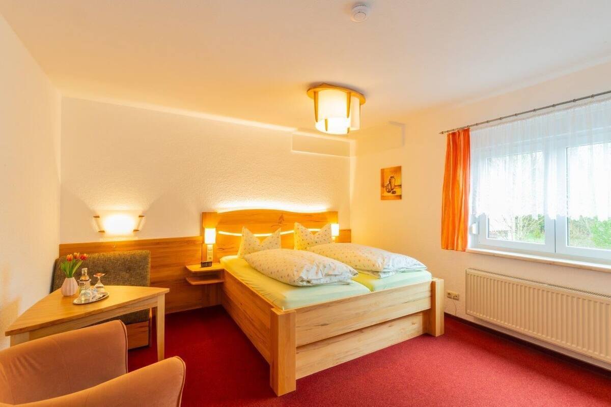 A hotel room with a bed, bedside table, lamp, and a window with curtains.