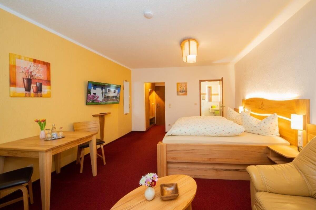 A hotel room with a bed, a desk, a chair, a sofa, and a small table with a vase of flowers.