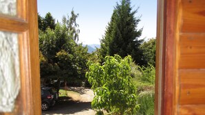 Varanda de madeira com vista para um jardim, um carro estacionado e uma montanha ao longe.