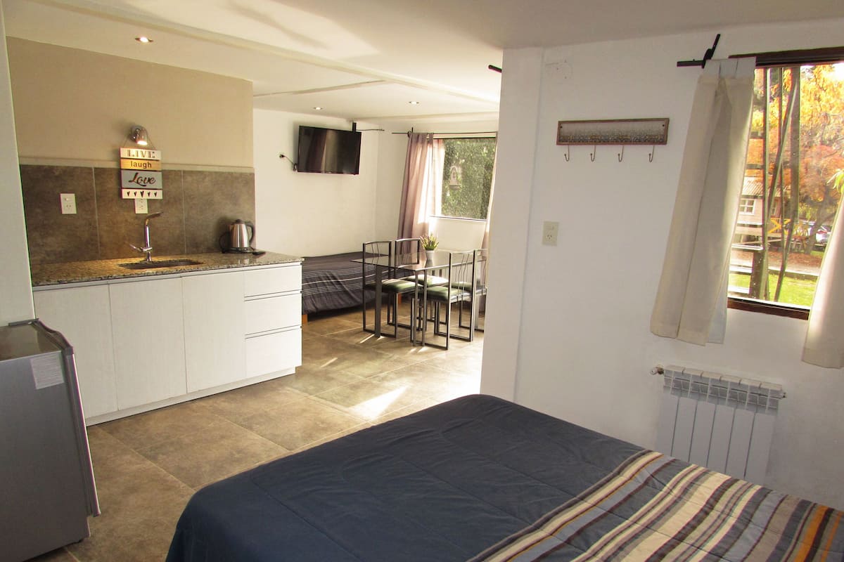 Habitación compacta con cama, kitchenette y zona de comedor.