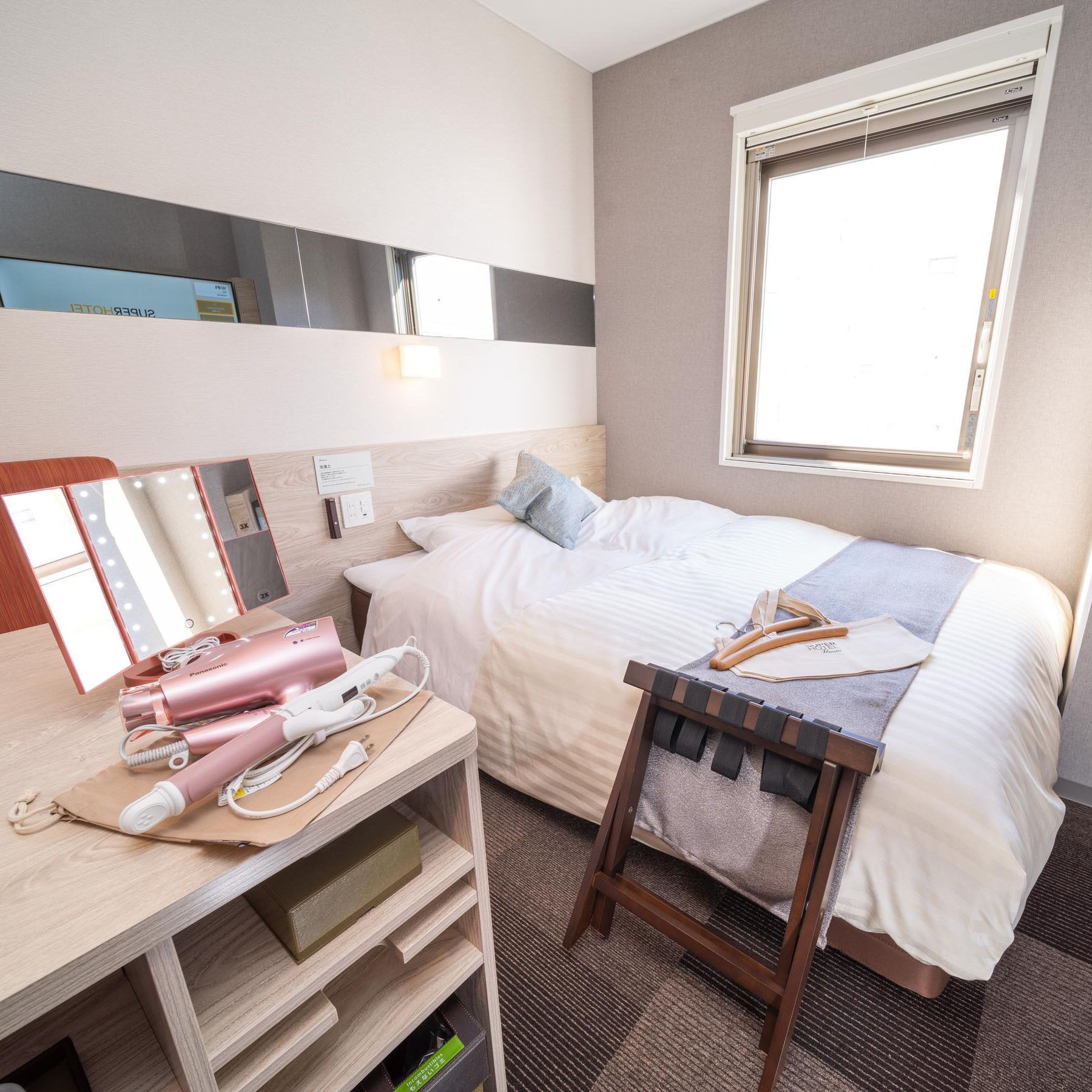 Habitación de hotel con cama, mesita de noche, espejo y ventana.