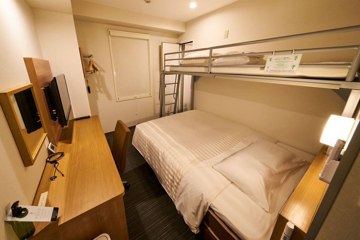 A compact hotel room with bunk beds, a desk with a computer, and a small table.
