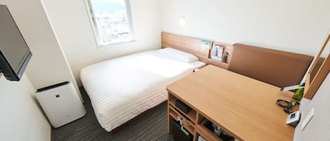 Habitación de hotel compacta con cama, escritorio, refrigerador pequeño, cesto de basura y ventana con vista a la ciudad.
