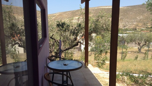 A covered outdoor seating area with a table and chairs, overlooking a hilly landscape. - Alex's Studio (Heraklion)