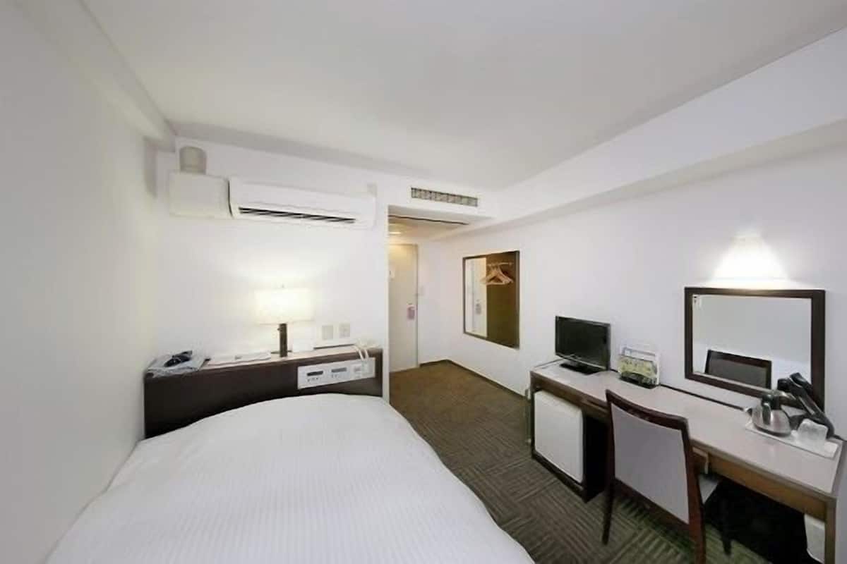 Ein Hotelzimmer mit Bett, Schreibtisch, Stuhl, Fernseher und Spiegel.
