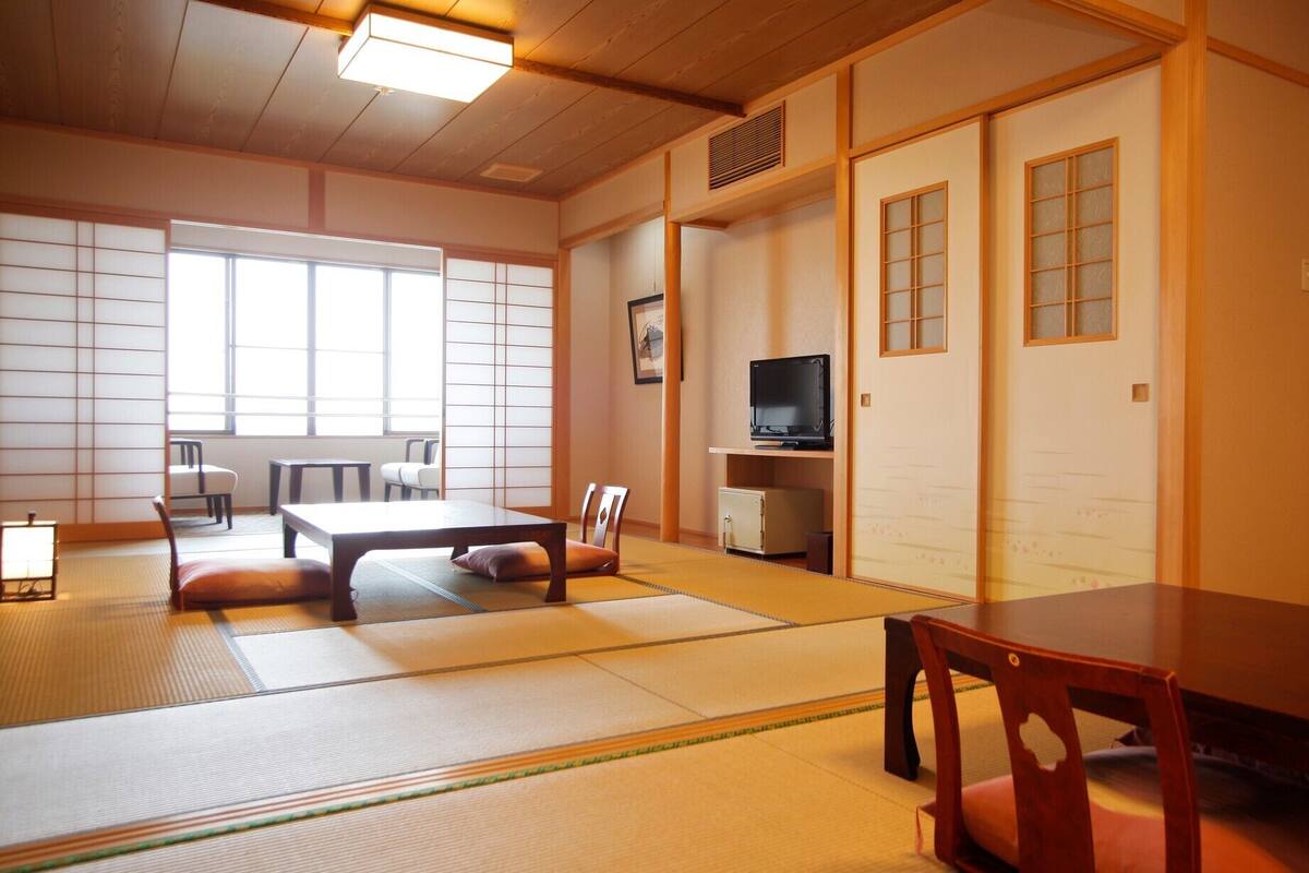 A traditional Japanese room with tatami flooring, a low table, chairs, a television, and sliding doors.