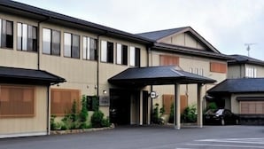 A multi-story hotel with a covered entrance, a parking lot, and a car parked outside. - Ikadaso Sanjo (Shima)
