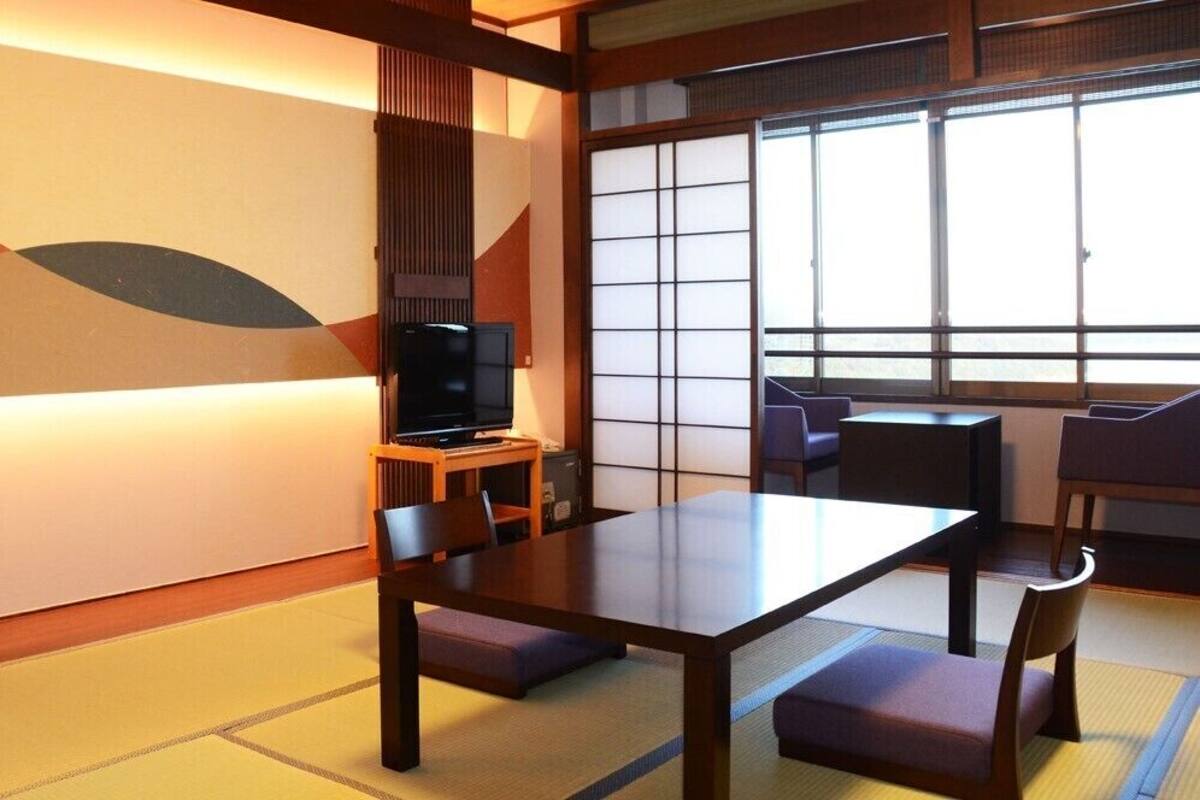 A traditional Japanese room with tatami flooring, a low table, and a television on a wooden stand.