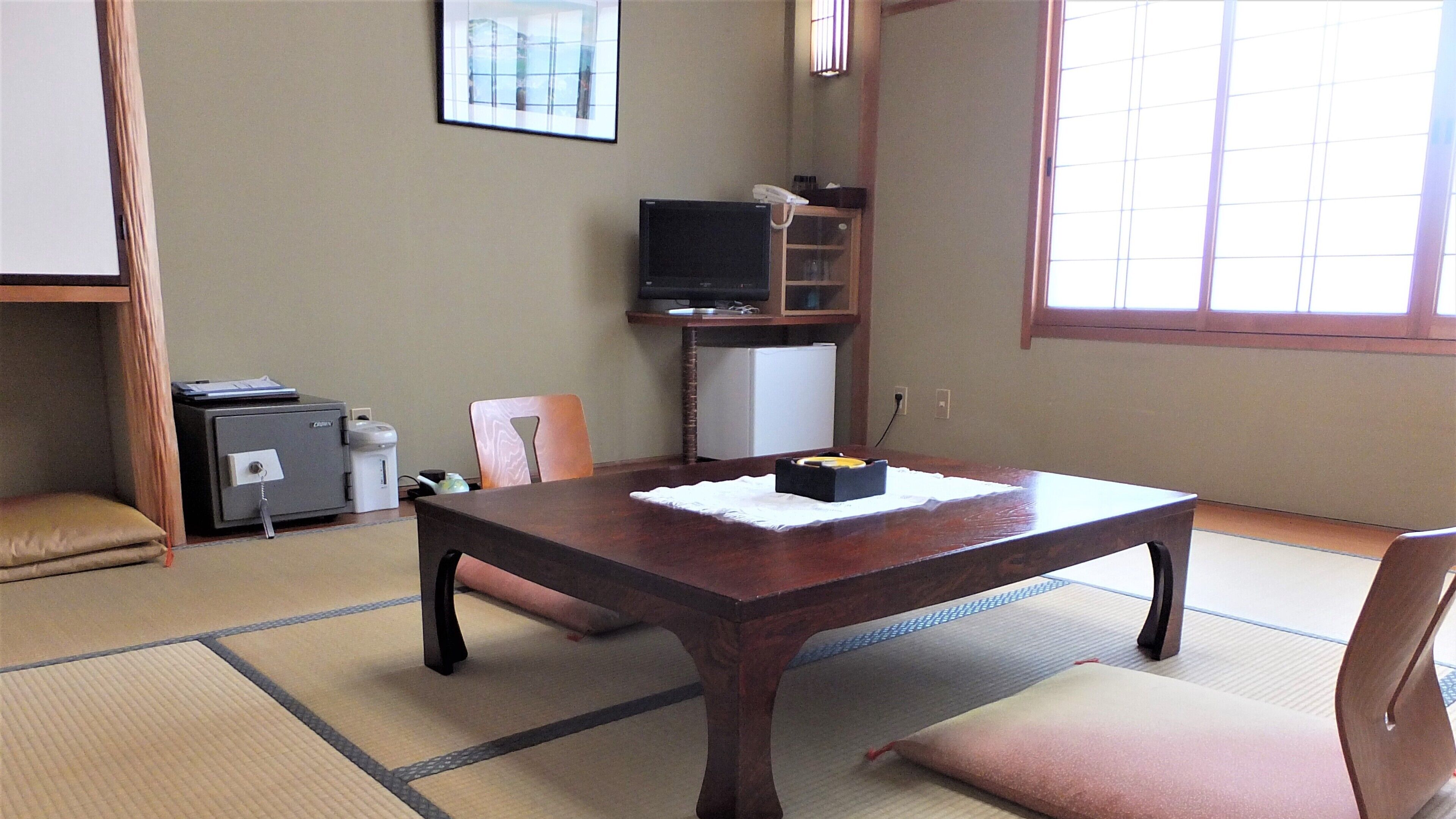 A traditional Japanese room with tatami flooring, a low table, a television, and a refrigerator.