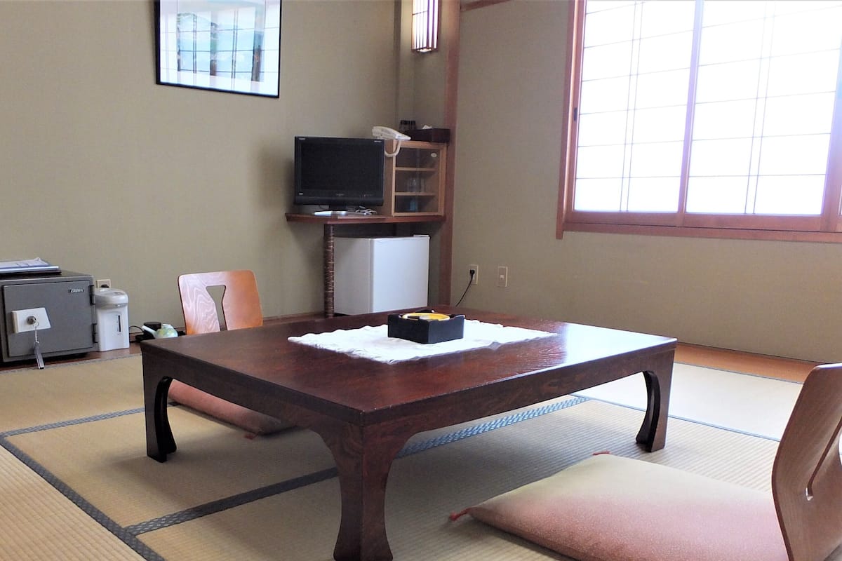 A traditional Japanese room with tatami flooring, a low table, a television, and a refrigerator.