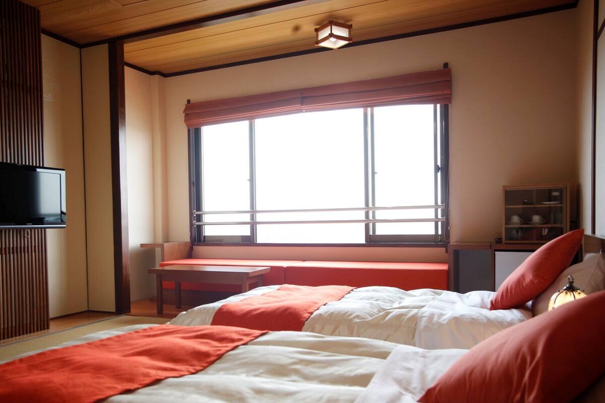 A bedroom with a bed, a desk, a TV, and a window with curtains.
