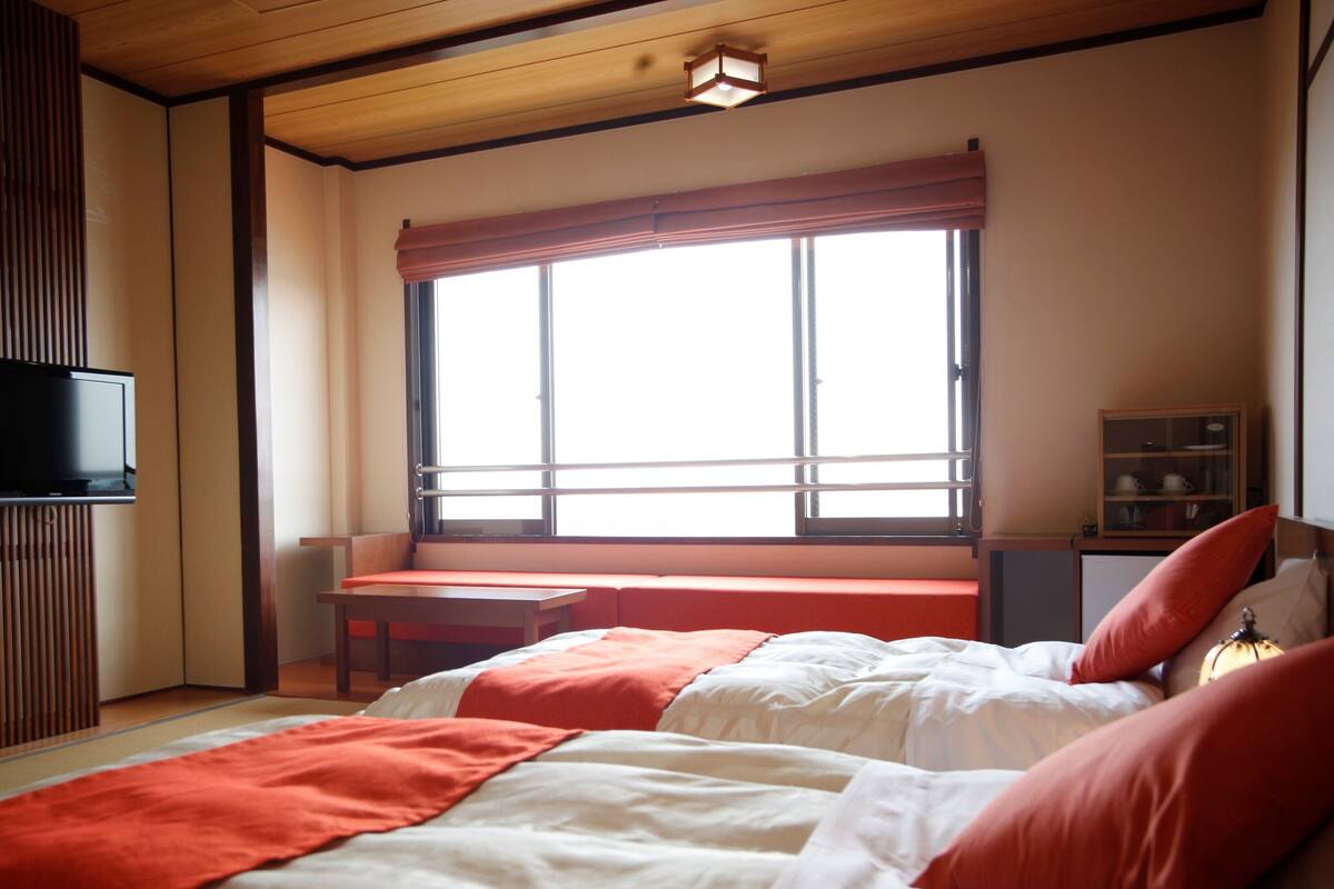 A bedroom with a bed, a TV, a window with a view, and a desk.