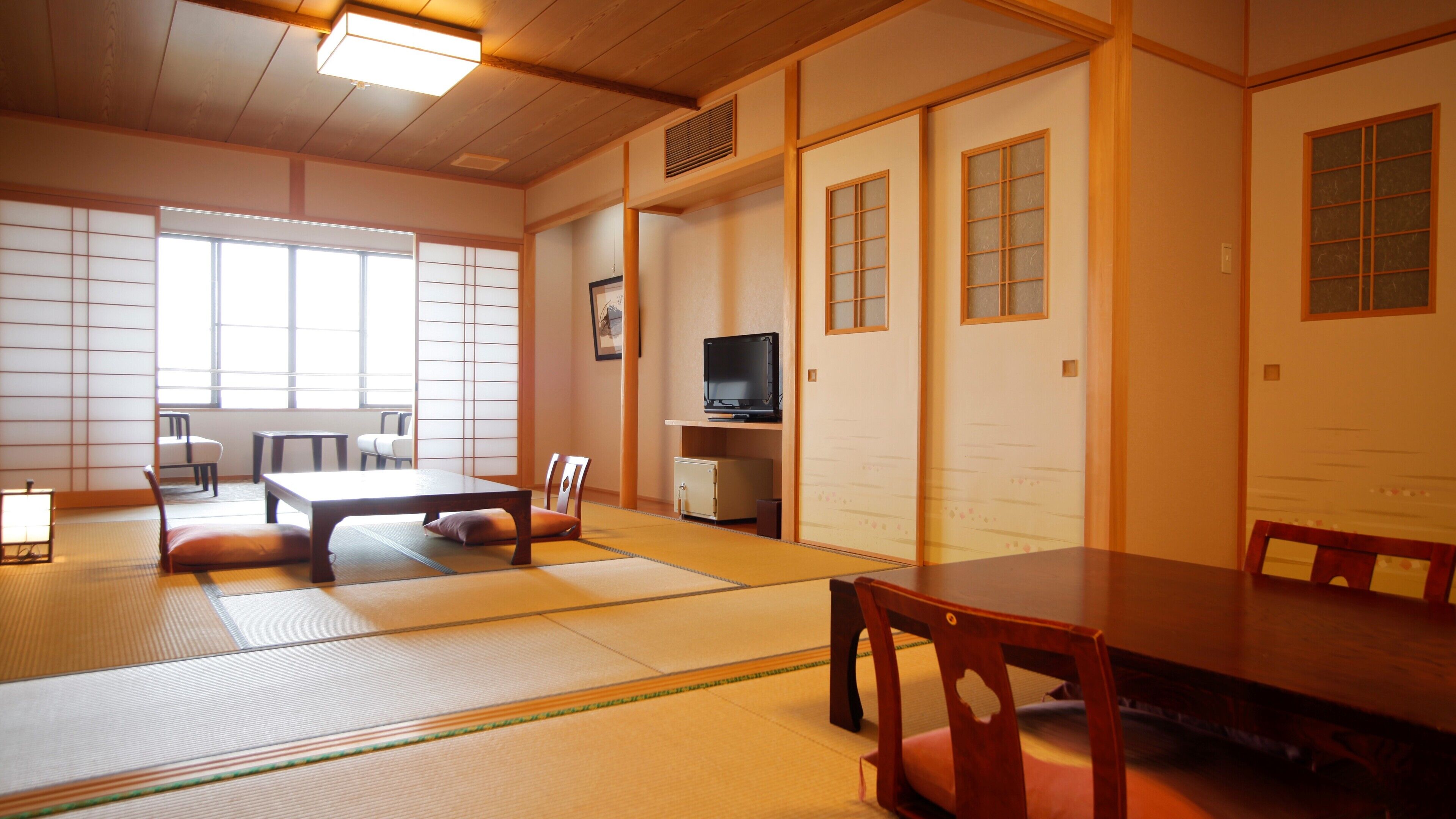 A traditional Japanese room with tatami flooring, a low table, chairs, a television, and sliding doors.