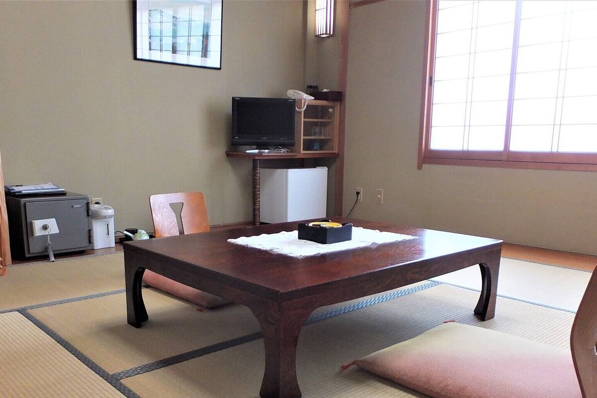 A room with tatami flooring, a wooden table, a television, a refrigerator, and a cabinet.