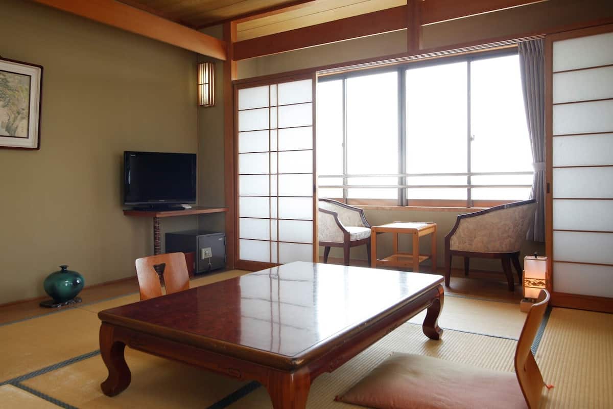 A traditional Japanese room with tatami flooring, a low table, chairs, a television, and a sliding door.