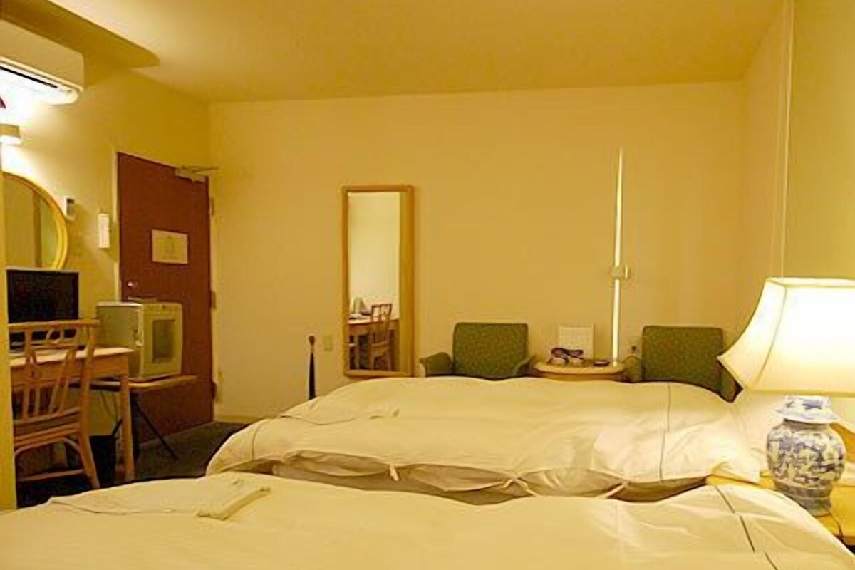 Ett hotellrum med två sängar, ett skrivbord med en stol, en spegel och ett nattduksbord med en lampa.