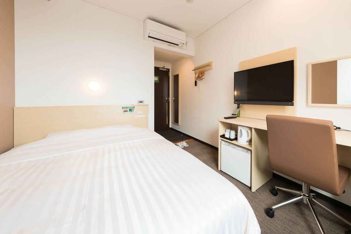 Hotellihuone, jossa on sänky, työpöytä tuolilla, televisio ja pieni keittonurkkaus.