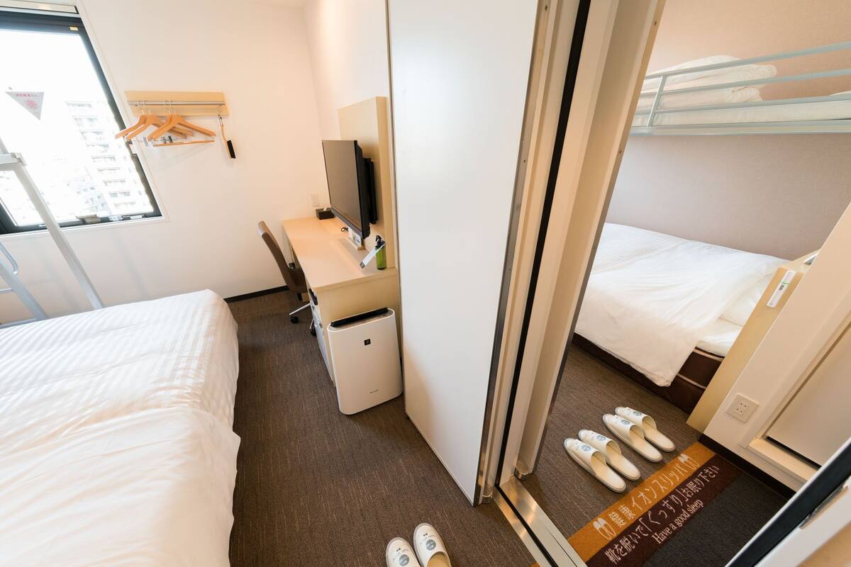 Hotellihuone, jossa on sänky, työpöytä tietokoneella, peili ja vaatekaappi.