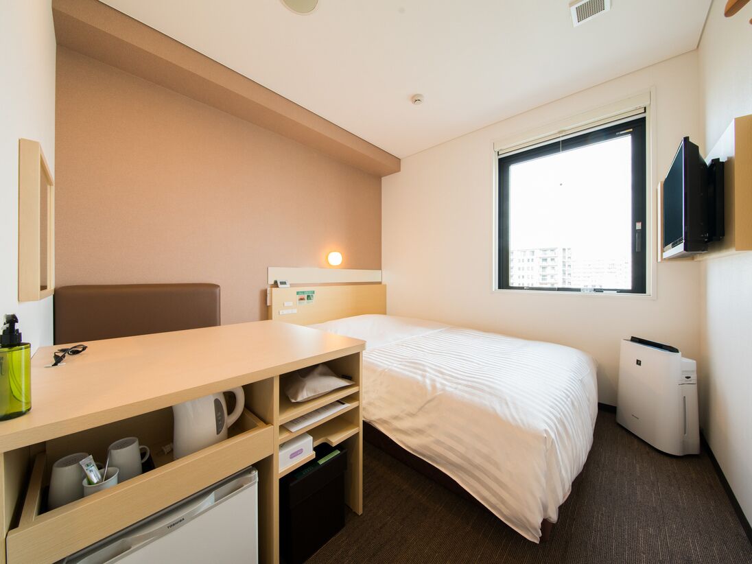 Une chambre d’hôtel comprenant un lit, un bureau avec des rangements, une télévision et une fenêtre.