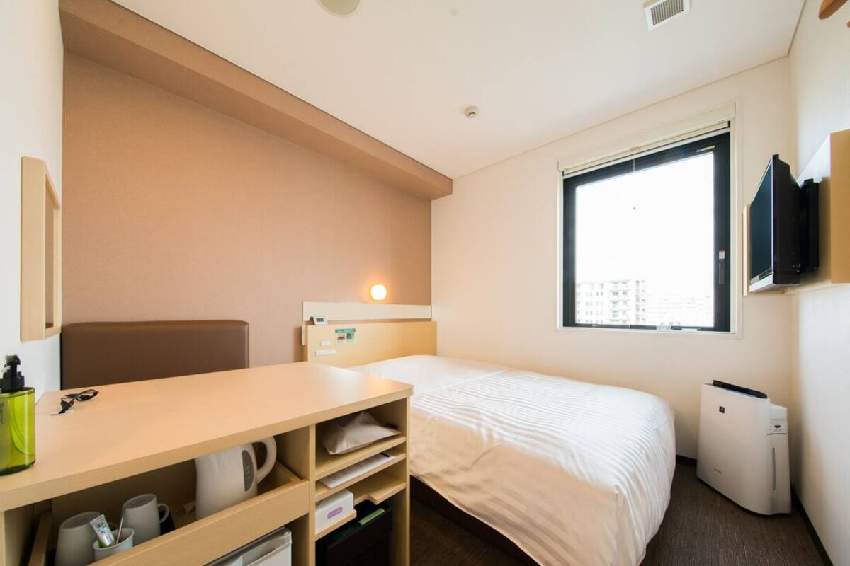 Hotellihuone, jossa on sänky, työpöytä säilytystilalla, televisio ja ikkuna.
