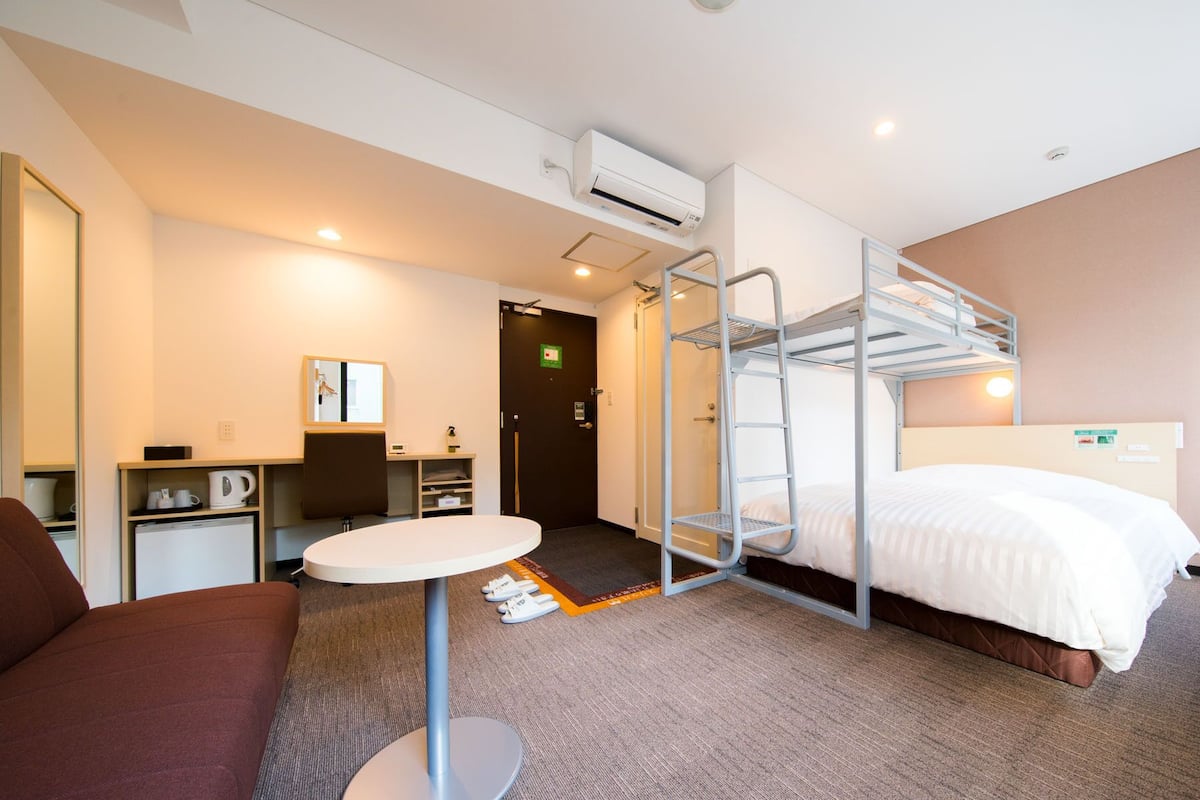 Hotellihuone, jossa on kerrossänky, pyöreä pöytä, sohva, työpöytä tuolilla ja pieni keittokomero.