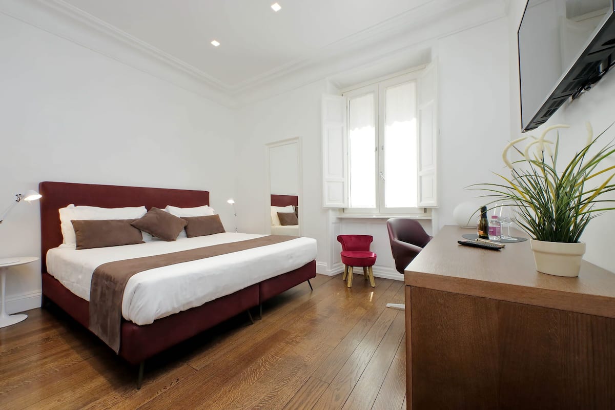 A modern bedroom with a large bed, a desk, a chair, and a potted plant.