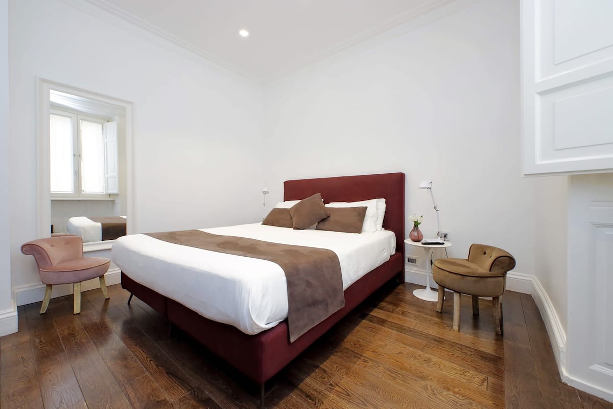 A bedroom with a large bed, two chairs, a small table, and a window.