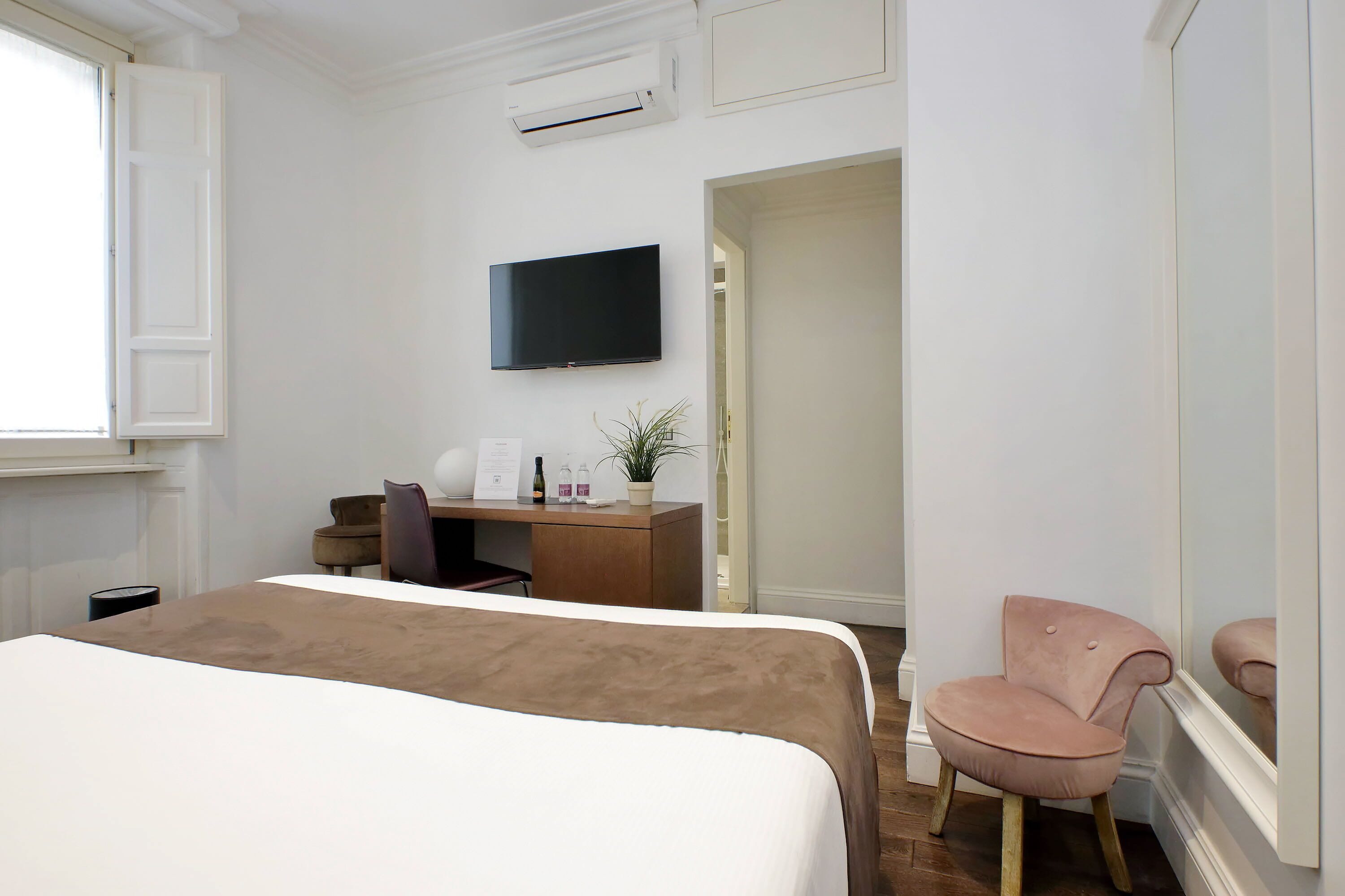 A hotel room with a bed, a desk, a chair, a television, and a potted plant.