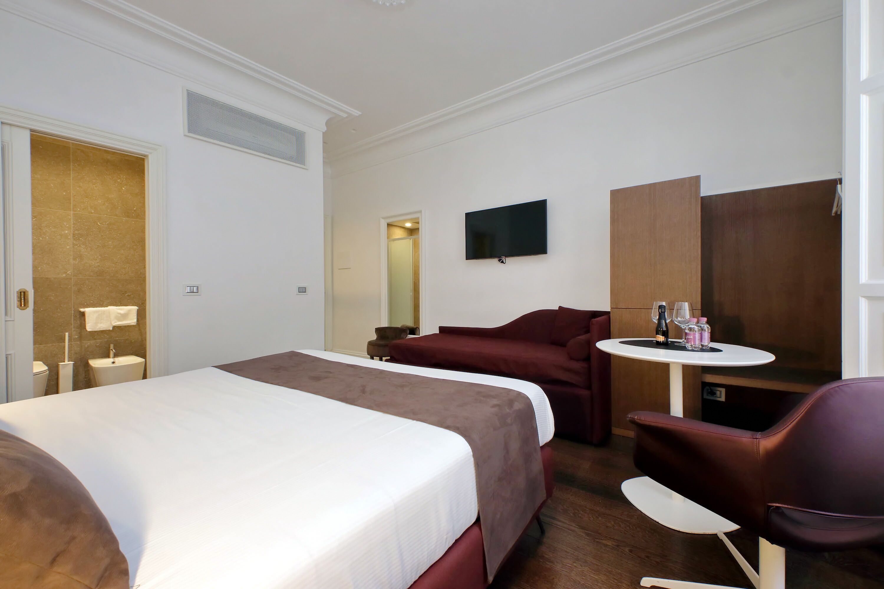 Una habitación de hotel con una cama grande, un escritorio, una silla, un televisor y una mesita con bebidas.