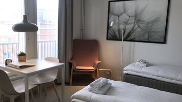 A hotel room with a desk, chair, two beds, a large window, and a wall-mounted artwork.