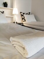 A neatly made bed with a folded white towel, a bedside lamp, and a pillow with a geometric pattern.