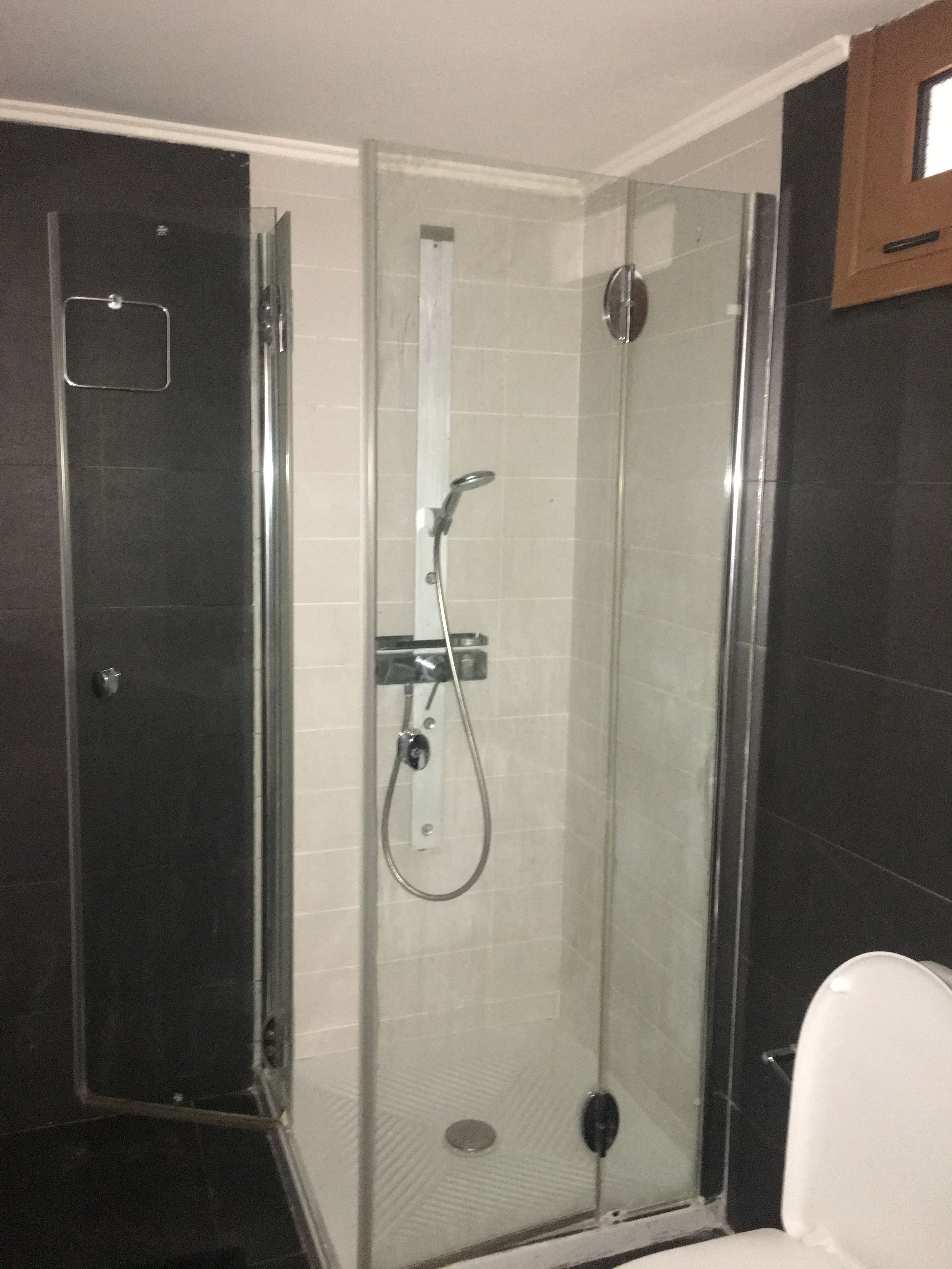 Un box de ducha con paredes de vidrio, un cabezal de ducha de mano y un panel de control en la pared.