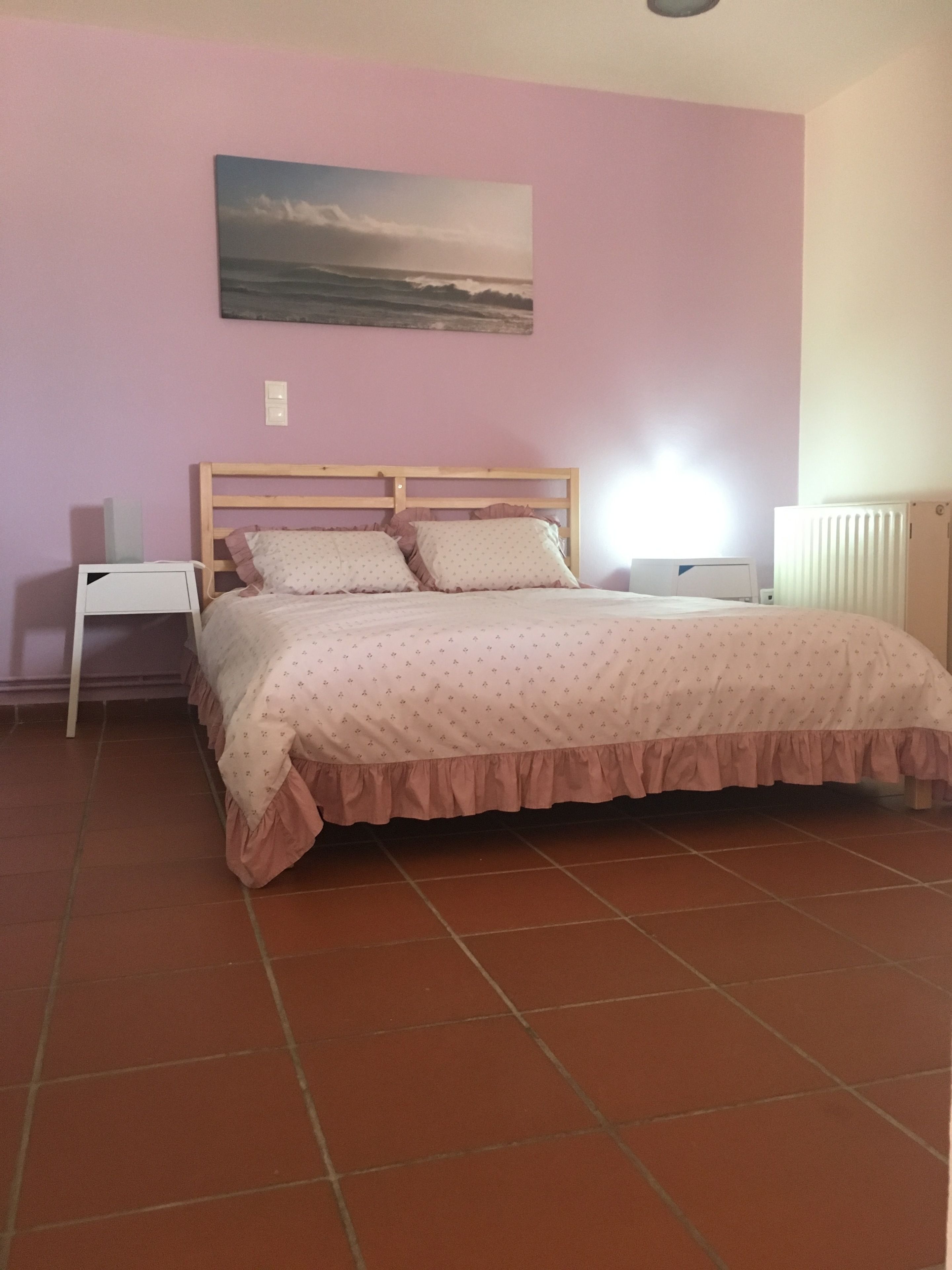 A bedroom with a bed, a nightstand, a wall-mounted lamp, and a radiator.