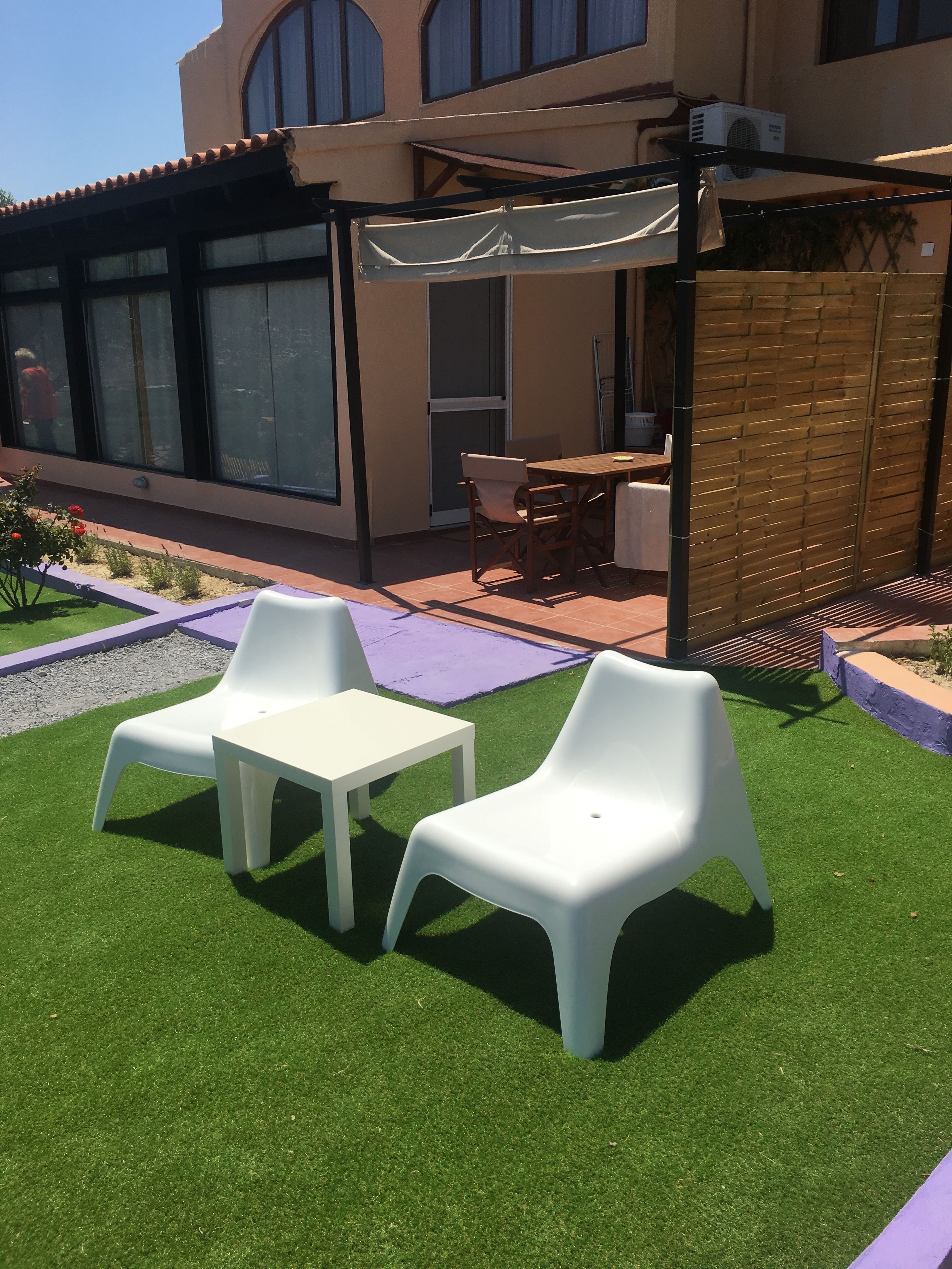 A patio with artificial grass, two white plastic chairs, and a small table.