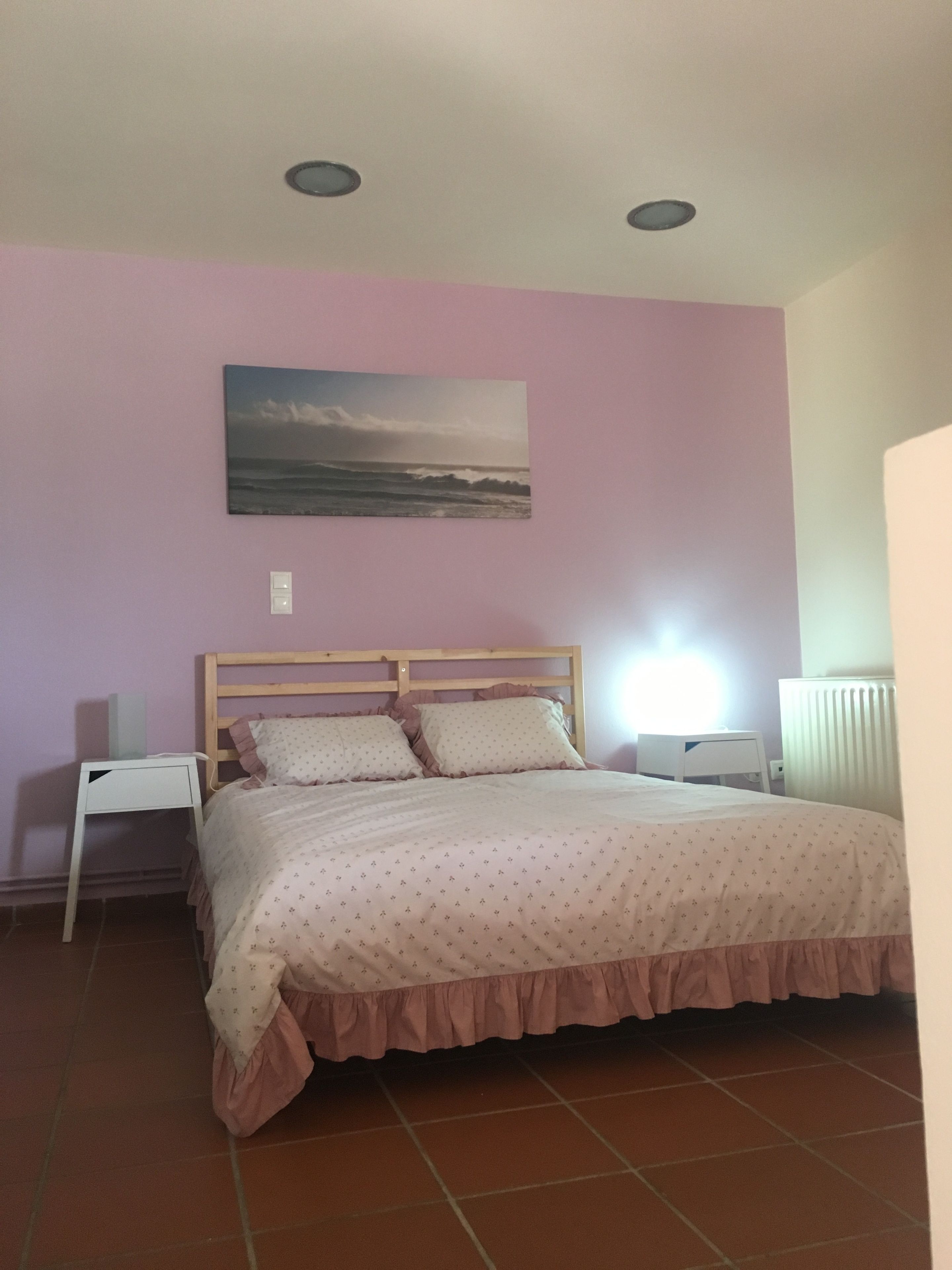 Une chambre à coucher avec un lit, une table de chevet, un tableau accroché au mur et un radiateur.