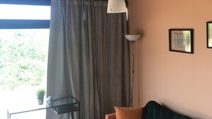 Una sala de estar acogedora con techo de madera, un sofá con cojines naranjas, una lámpara de pie y vistas al verdor exterior.