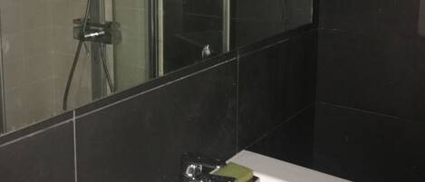 Ein modernes Badezimmer mit einem weißen Waschbecken, einer Glasdusche und einem großen Spiegel.