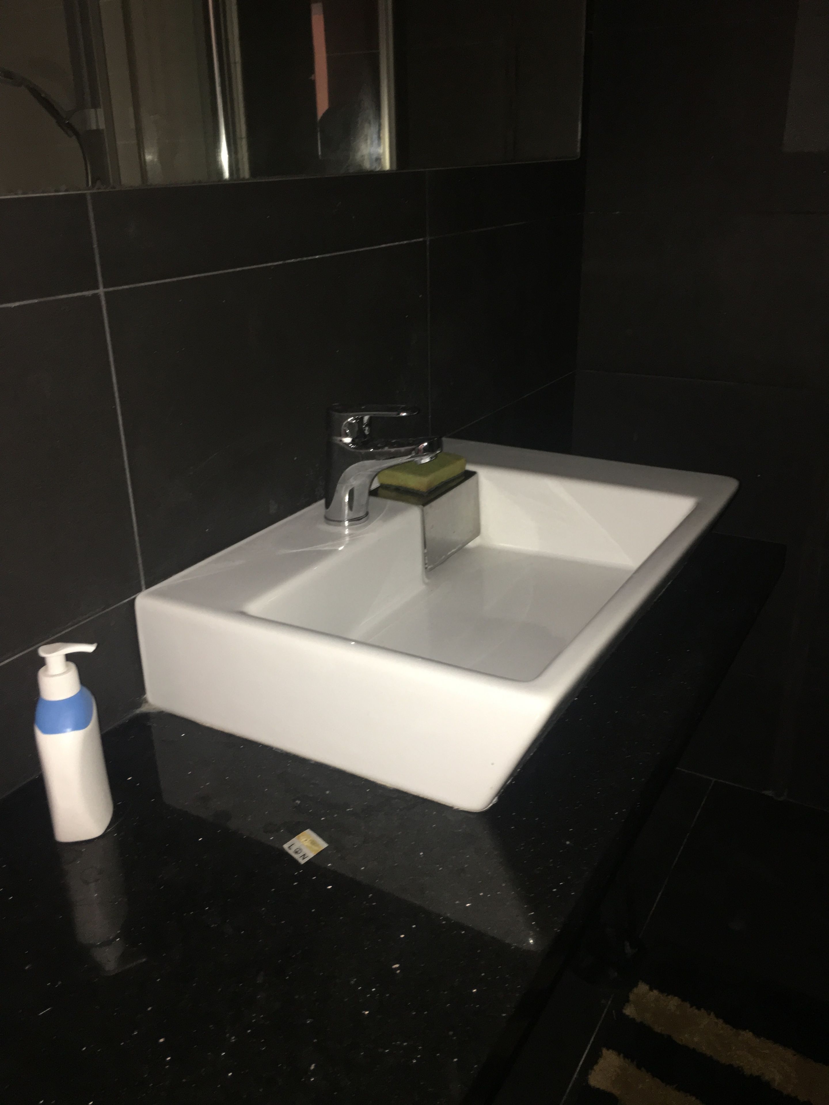 Une salle de bain avec un lavabo blanc, un miroir et un distributeur de savon, le tout posé sur un comptoir noir.