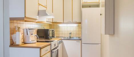 A compact kitchen with white cabinets, a microwave, a coffee maker, and a sink.
