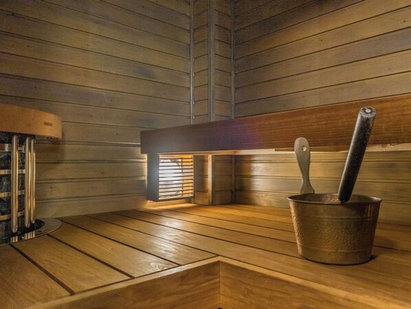 A sauna room with wooden benches, a metal bucket, and a wooden bench with a metal handle.