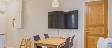Un'area pranzo con un tavolo in legno, sedie nere, un televisore montato a parete e una porta in legno.