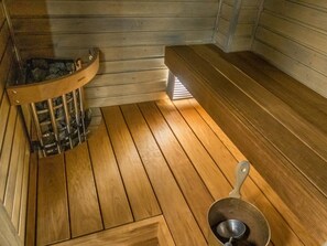 A sauna room with wooden benches and a metal bucket.
