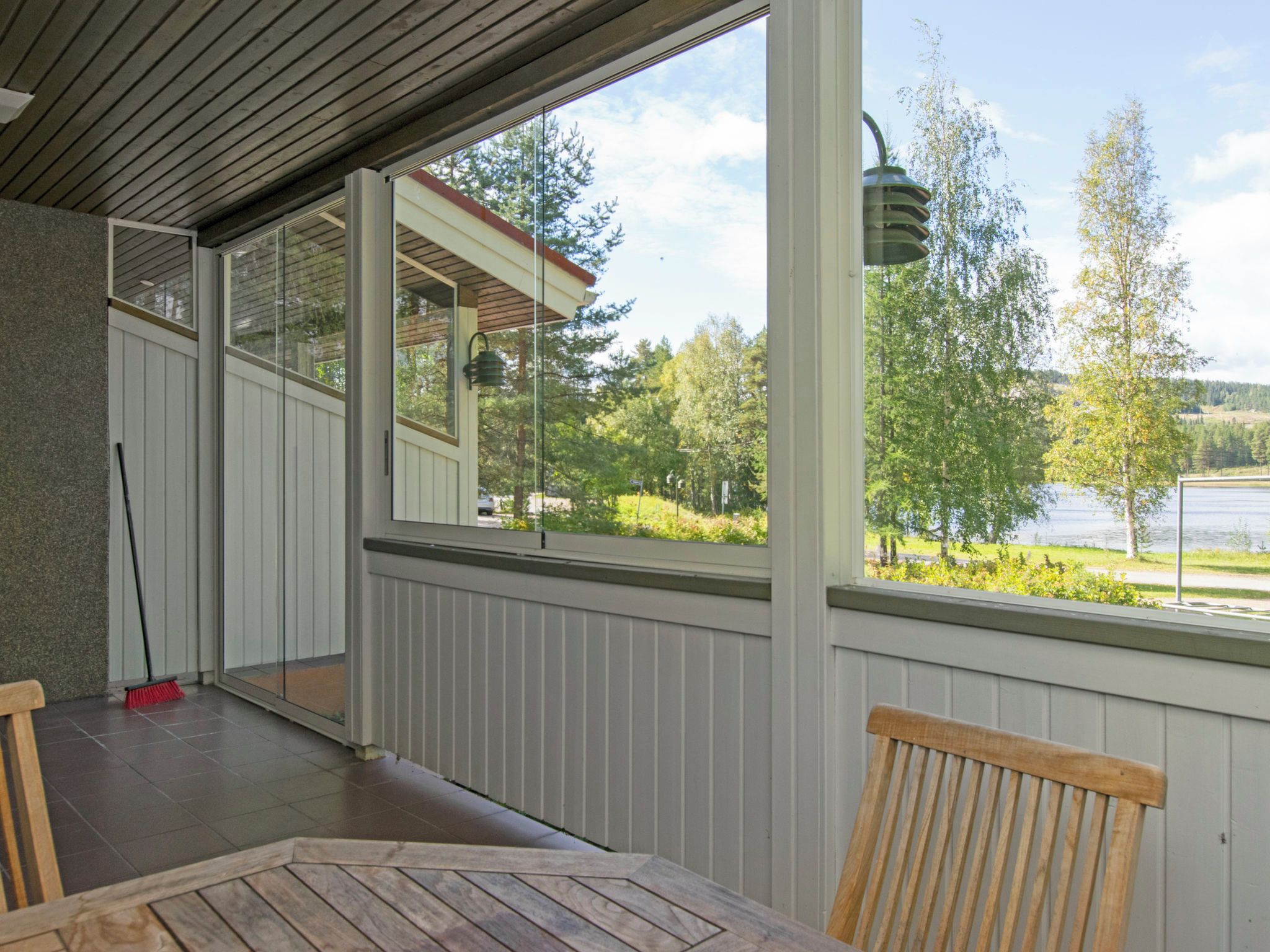 A covered outdoor area with a table and chairs, a broom, and a view of a lake and trees.